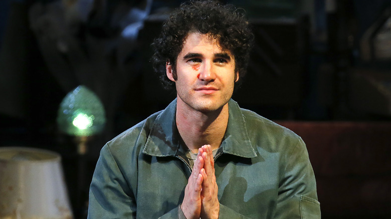 Darren Criss with hands in prayer, looking on
