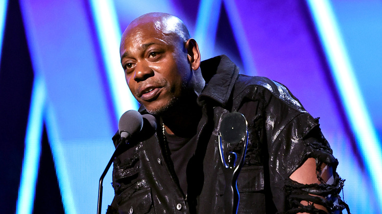 Dave Chappelle talking into a microphone at an awards show.