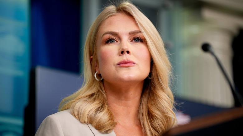 Karoline Leavitt stands before microphone with pursed lips