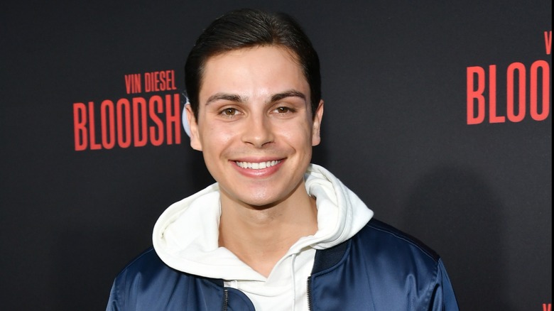 Sporting a navy blue jacket and a white hoodie, Jake T. Austin pastes a wide smile.