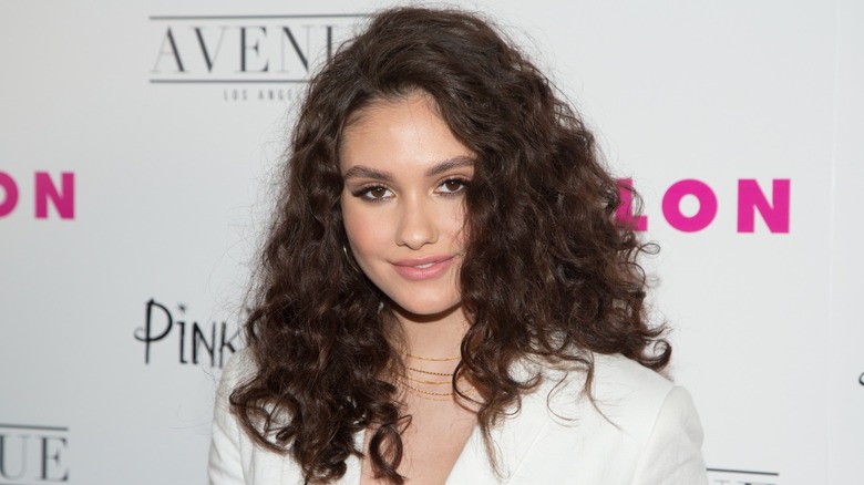 Wearing a wavy hairdo and a white number, Ronni Hawk' gives the camera an intense stare.