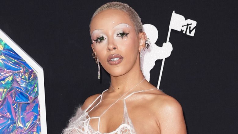 Doja Cat wearing a white spiderweb-type gown with silver sparkly make-up and shaved head