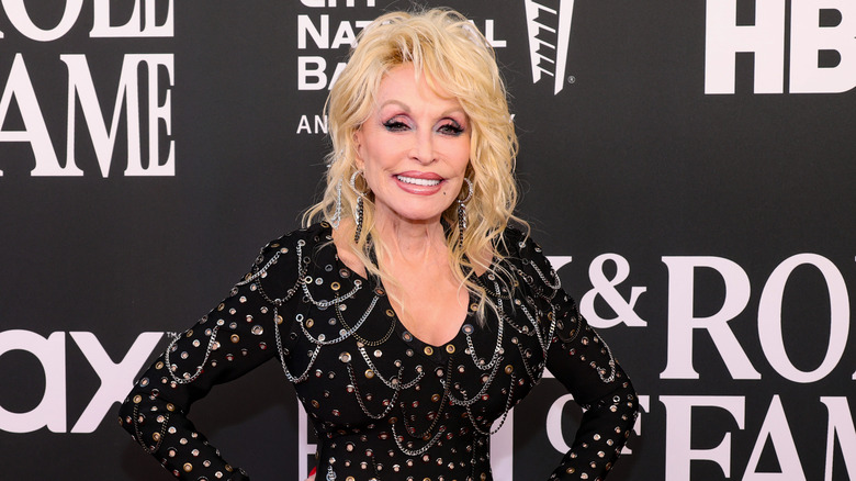 Dolly Parton posing with her hands on her hips in a glitzy black dress at the Rock 'n Roll Hall of Fame