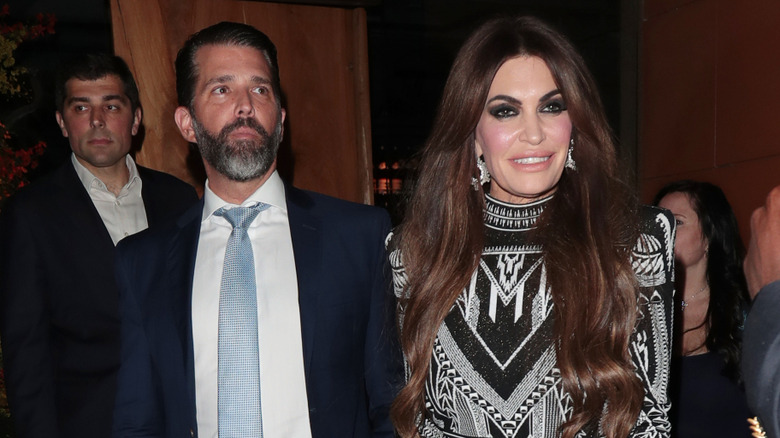 Donald Trump Jr. wearing suit with blue tie, Kimberly Guilfoyle wearing black and white patterned dress