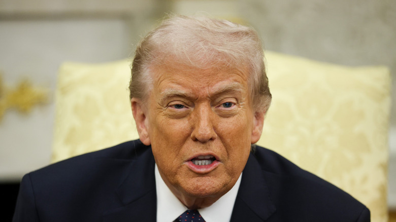 Donald Trump speaking in the Oval Office in a black suit