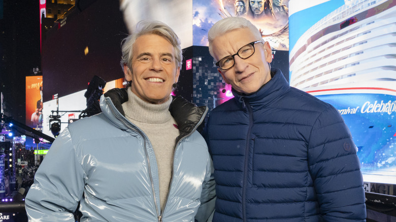 Andy Cohen and Anderson Cooper smiling while posing together in puffer jackets on New Year's Eve