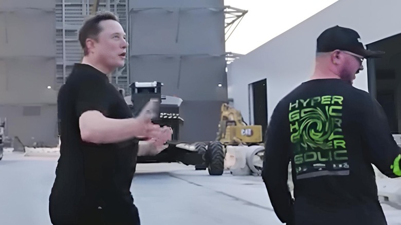 Elon Musk showing off a tubby tummy in a black shirt