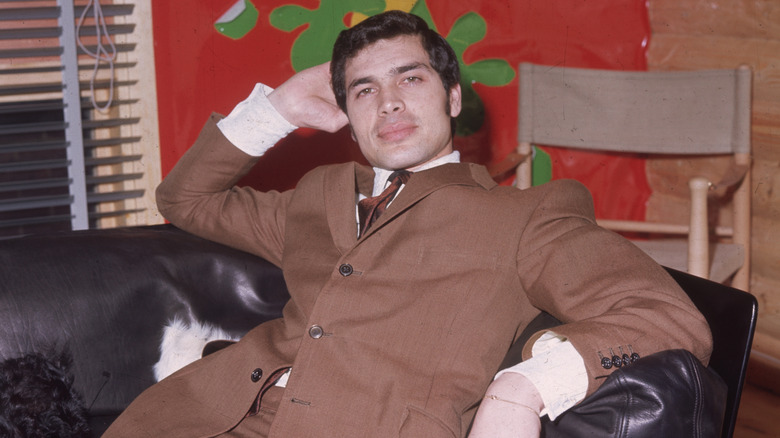 Engelbert Humperdinck wearing a light brown suit and sitting on a leather couch