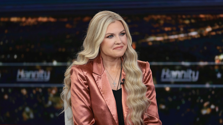 Erika Kirk smiling in a salmon pink blazer with a black shirt underneath