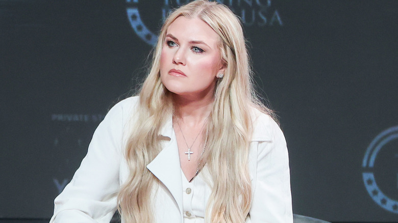 Erika Kirk speaking on stage in April 2026 in a white blazer with a white top underneath
