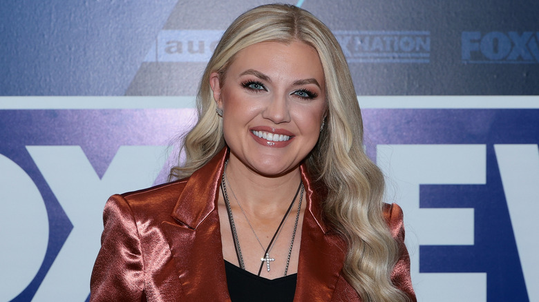 Erika Kirk smiling while posing in a shiny peach blazer