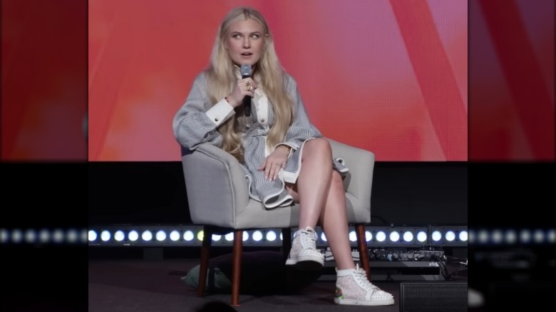 Erika Kirk seated and holding a microphone on stage in a shirt dress