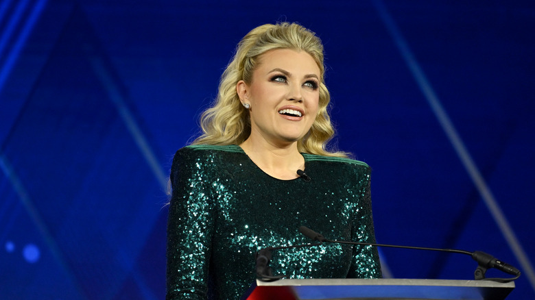 Erika Kirk smiling while standing in front of a microphone in a sparkly green dress