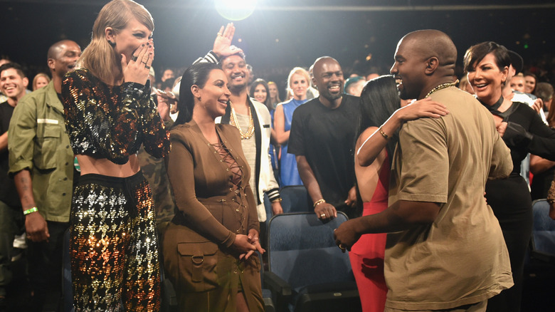Taylor Swift and Kim Kardashian smiling at Kanye West