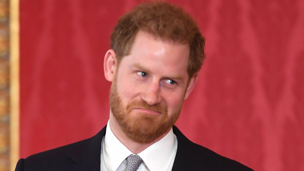 Prince Harry shrugging and pulling a face in a dark blue suit