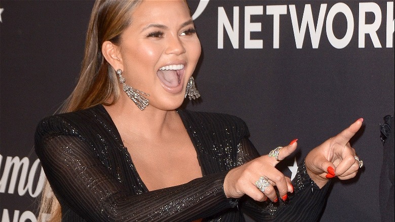 Chrissy Teigen pointing and laughing on a red carpet