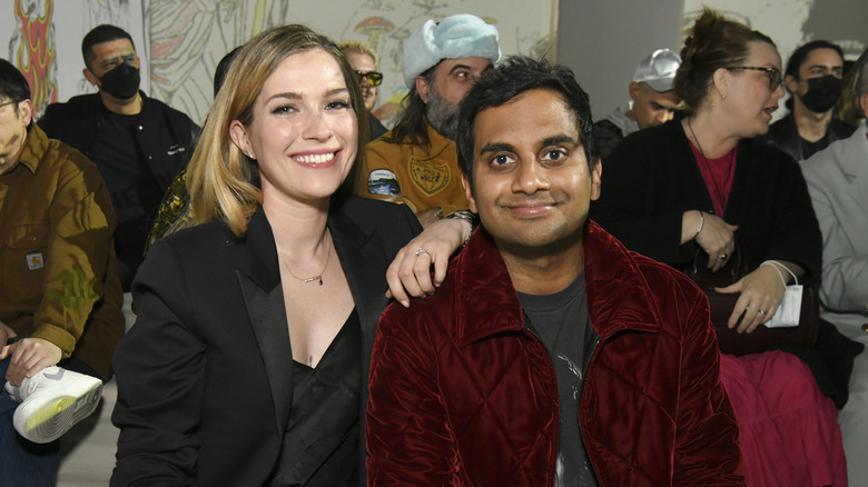 Aziz Ansari and Serena Skov Campbell smile at a runway show in 2022