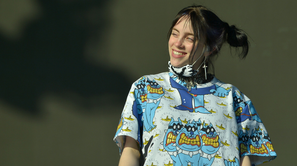 Billie Eilish smiling and wearing a mask under her chin