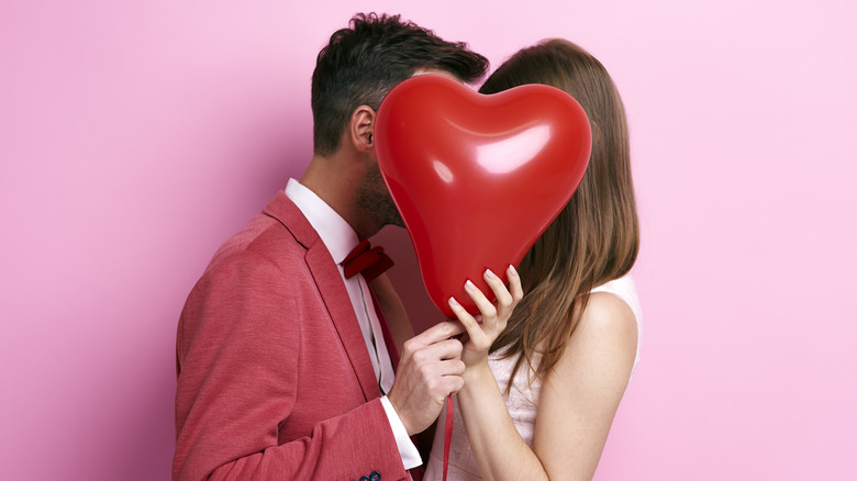 Couple kissing behind heart balloon