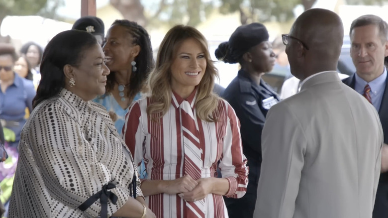 Melania Trump smiling in a red and white striped dress in Africa