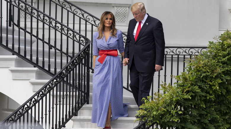 Melania Trump wearing a Ralph Lauren gingham dress while walking down a staircase hand in hand with President Trump