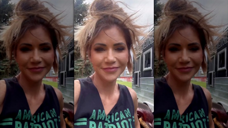 A screenshot of Kristi Noem outdoors with her hair pulled up in a high, messy bun.