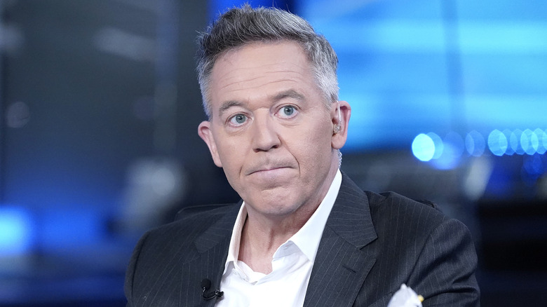 Greg Gutfeld sitting at a desk with pursed lips