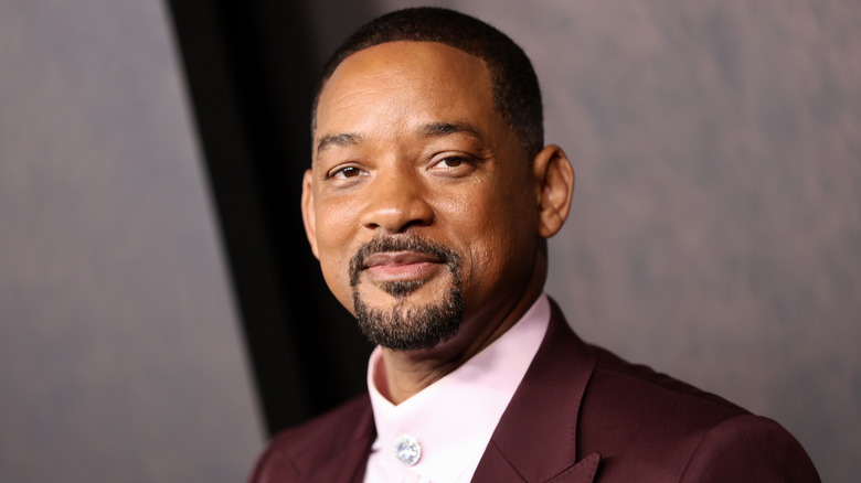 Will Smith smiles slightly in a maroon jacket and pink shirt.
