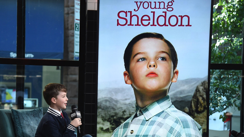 Iain Armitage sitting in front of a poster of him as Young Sheldon during an interview