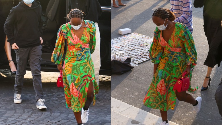 Zahara Jolie wears white sneakers and a bright green dress with a colorful leaf print outdoors in France.