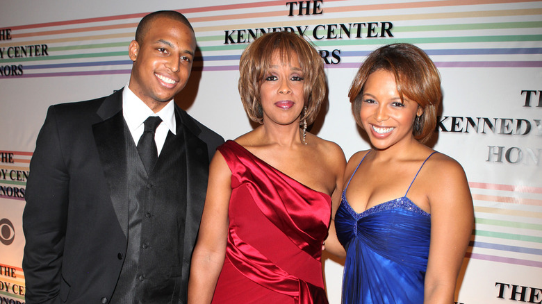 Gayle King wearing a shiny red dress at an event with William Bumpus Jr. and Kirby Bumpus.