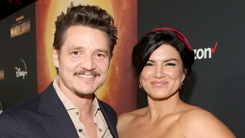 Pedro Pascal, smiling, in a suit, red carpet; Gina Carano, smiling, hair up, strapless gown