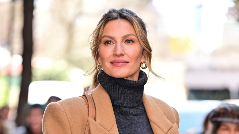 Gisele Bündchen smiling in a camel coat and a dark grey turtleneck