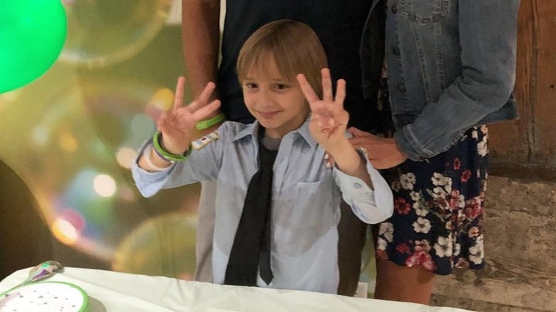 A young Duke Rancic sporting bangs and a blue shirt making hand gestures