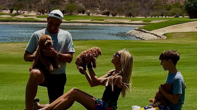 Bill, Giuliana and Duke Rancic holding puppies on a golf course with big smiles on their faces
