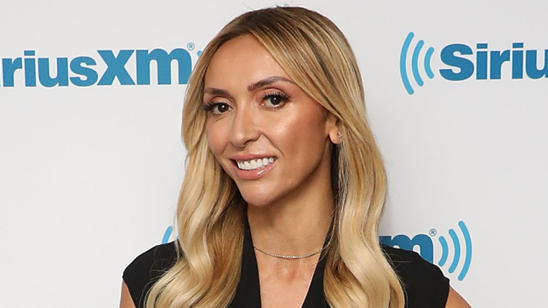 Giuliana Rancic wearing a black top and long blonde waves with a small gold jeweled necklace
