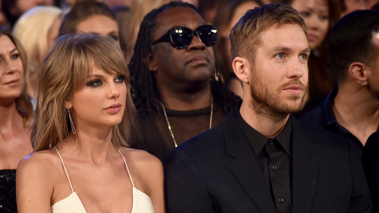 Taylor Swift wearing a strappy white jumpsuit with Calvin Harris wearing a black jacket and black button-down shirt