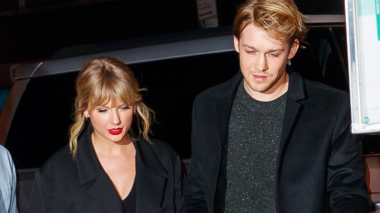 Taylor Swift wearing a black jacket and red lipstick with Joe Alwyn wearing a black jacket and grey sweater