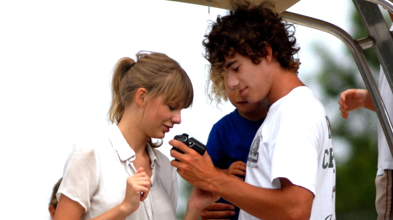 Taylor Swift wearing a white button down blouse and Conor Kennedy looking at a camera wearing a white t-shirt