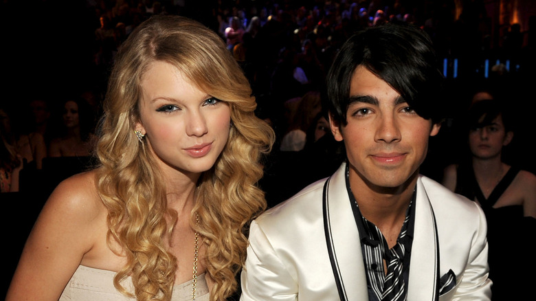 Taylor Swift wearing a white strapless dress and Joe Jonas wearing a white satin jacket and patterned tie