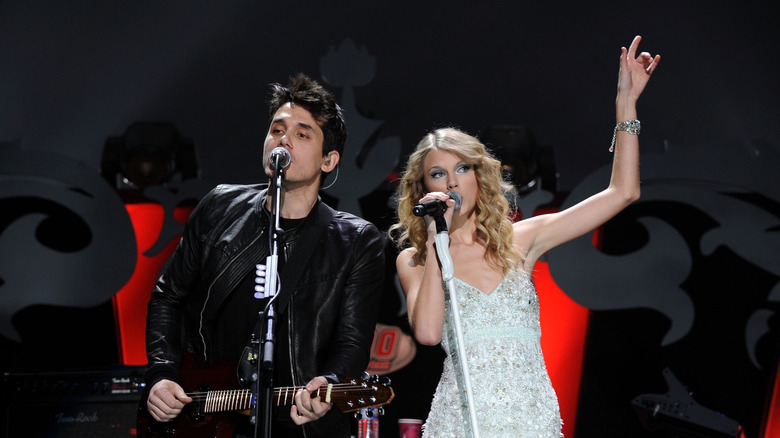 John Mayer wearing a black leather jacket and black t-shirt with Taylor Swift wearing a silver sparkling dress
