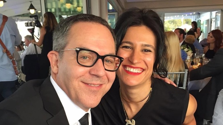 Greg Gutfeld and Elena Moussa smile sitting at a table