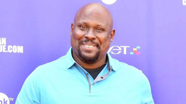 Dressed in a light blue shirt, Doc Farrow poses in front of a purple background.