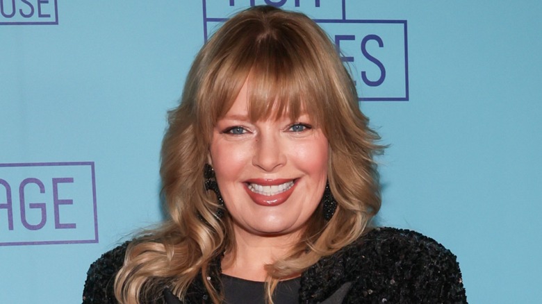 Wearing an all-black outfit, Melissa Peterman looks directly at the camera while smiling.