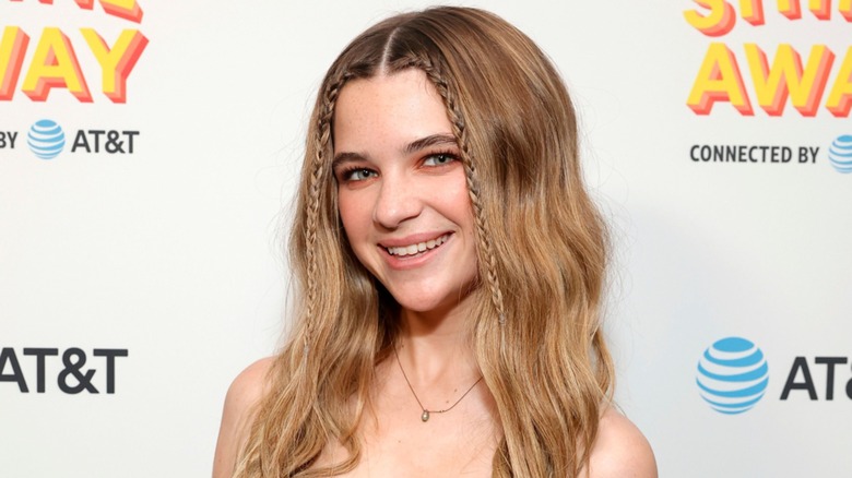 Sporting two front-row braids and parted hair, Raegan Revord has a wide smile.