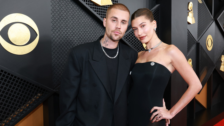 Hailey Bieber wearing an "ICE OUT" pin on her black dress and posing beside Justin Bieber at the Grammys.