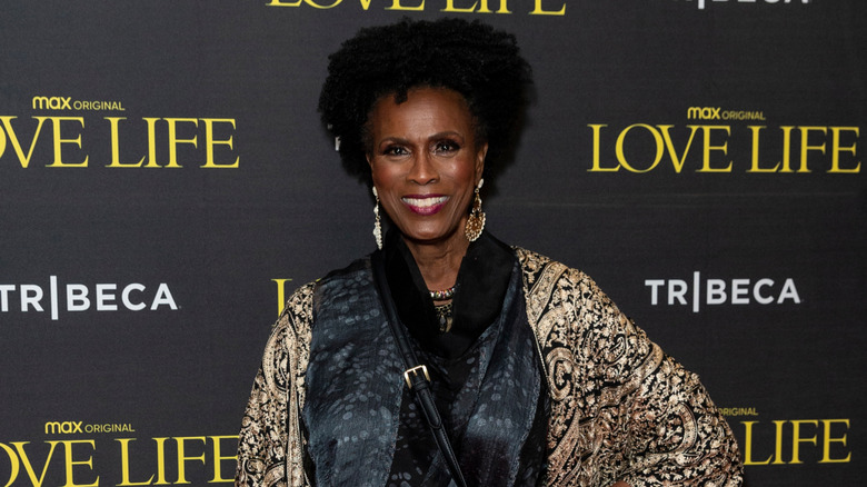 Janet Hubert smiles at a red carpet event against a black background.