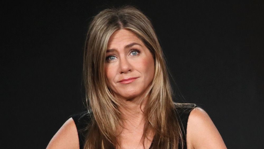 Jennifer Aniston in a black dress, shrugging
