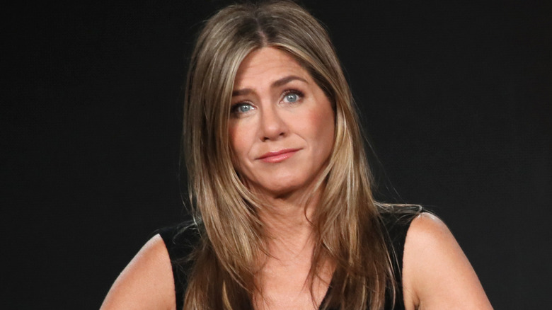 Jennifer Aniston in a black dress, shrugging