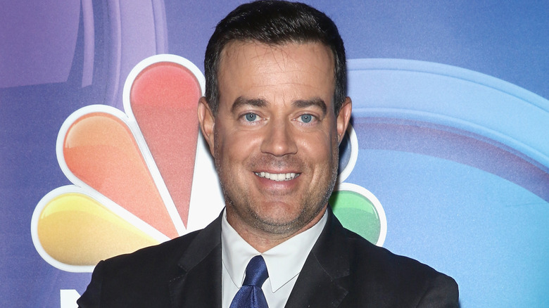 Carson Daly smiling in front of NBC logo